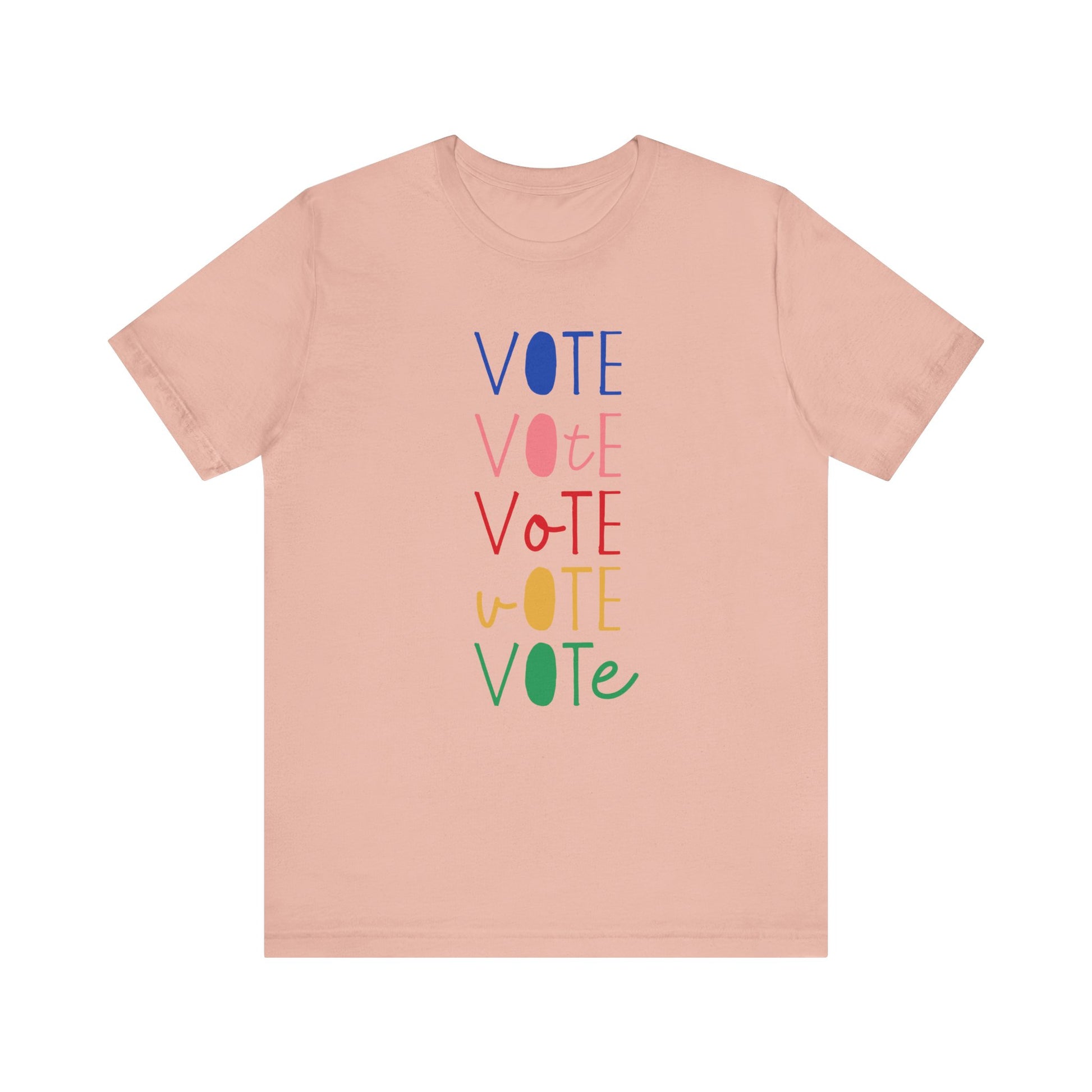 A peach short-sleeve t-shirt with a vertical graphic on the chest spelling 'VOTE' in alternating bright colors (blue, pink, red, yellow, green) with oval letterforms, shown on a plain white background.