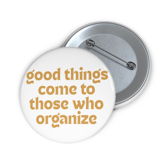 White pin button with 'good things come to those who organize' gold text