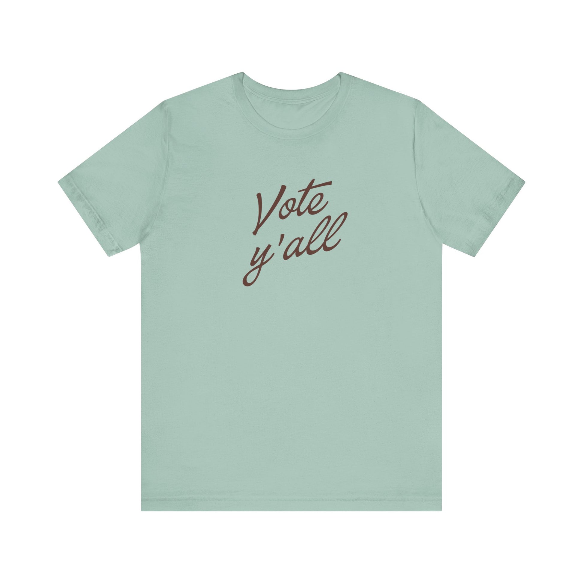 A sage green short-sleeve t-shirt with the phrase 'Vote y'all' printed in brown cursive script across the chest, displayed on a clean white background.