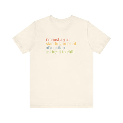 Beige t-shirt with colorful text "i'm just a girl, standing in front of a nation, asking it to chill"