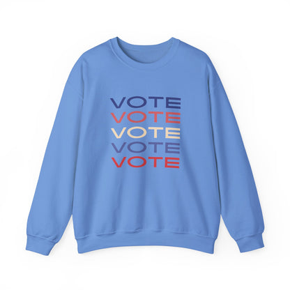 A light blue crewneck sweatshirt featuring a stacked graphic print of the word 'VOTE' in blue, red, and beige, displayed on a clean white background.
