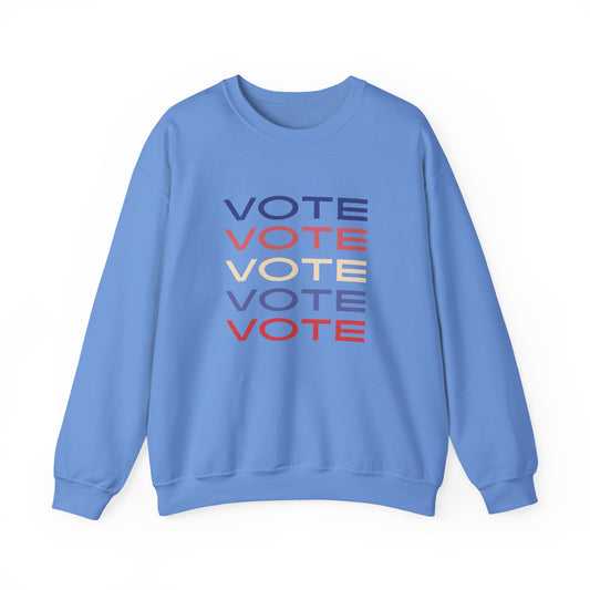 A light blue crewneck sweatshirt featuring a stacked graphic print of the word 'VOTE' in blue, red, and beige, displayed on a clean white background.