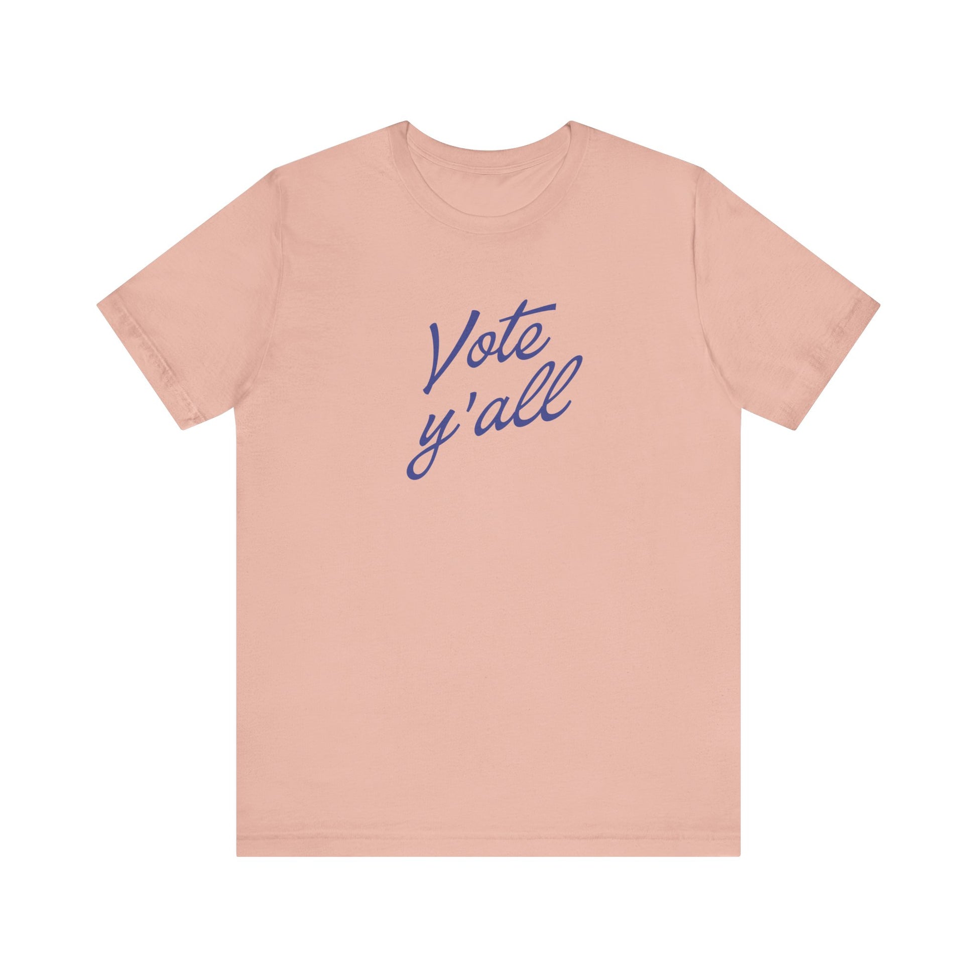 A light peach-pink short-sleeve t-shirt with the words 'Vote y'all' printed in a blue cursive script across the chest, displayed on a solid white background.