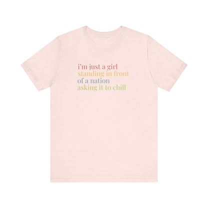 Pink t-shirt with colorful text "i'm just a girl, standing in front of a nation, asking it to chill"