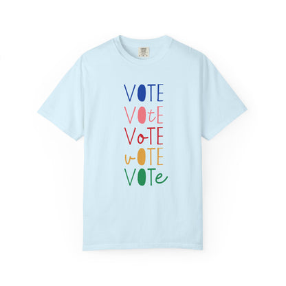 A light blue short-sleeve t-shirt with a vertical graphic spelling 'VOTE' in alternating blue, pink, red, yellow, and green colors, displayed on a clean white background.