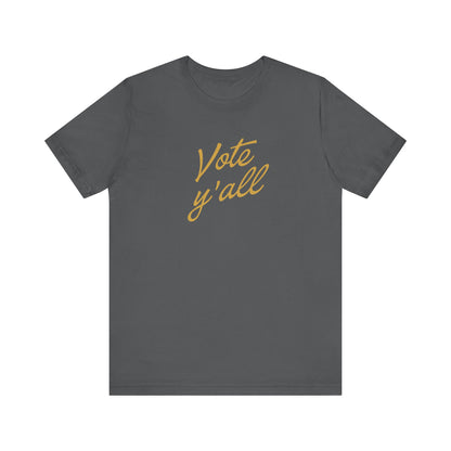 A dark gray crewneck t-shirt with 'Vote y'all' printed in a gold cursive script across the chest, displayed on a solid white background.