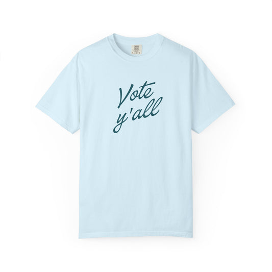 A light blue short-sleeve crewneck t-shirt with the words 'Vote y'all' printed in a dark teal cursive font across the chest, displayed on a clean white background.