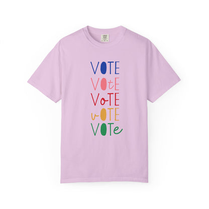 A light purple short-sleeve t-shirt with a vertical graphic spelling 'VOTE' in alternating blue, pink, red, yellow, and green colors, displayed on a clean white background.