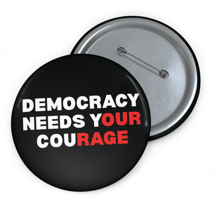 Black pin button with 'DEMOCRACY NEEDS YOUR COURAGE' white and red text