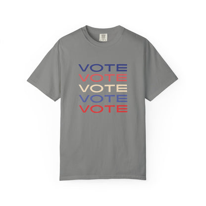 A gray short-sleeve crewneck t-shirt featuring a stacked graphic print of the word 'VOTE' in blue, red, and beige, displayed on a clean white background.