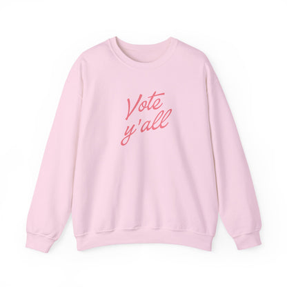 A light pink crewneck sweatshirt with the phrase 'Vote y'all' printed in a pink cursive font across the chest, displayed on a clean white background.