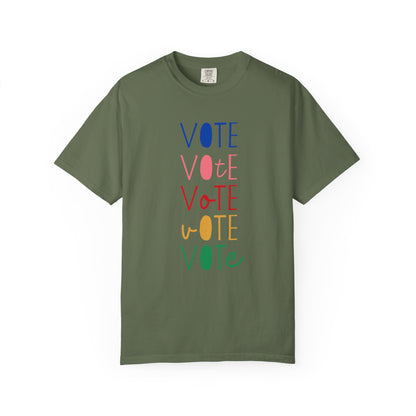 A military green short-sleeve t-shirt with a vertical graphic spelling 'VOTE' in alternating blue, pink, red, yellow, and green colors, displayed on a clean white background.