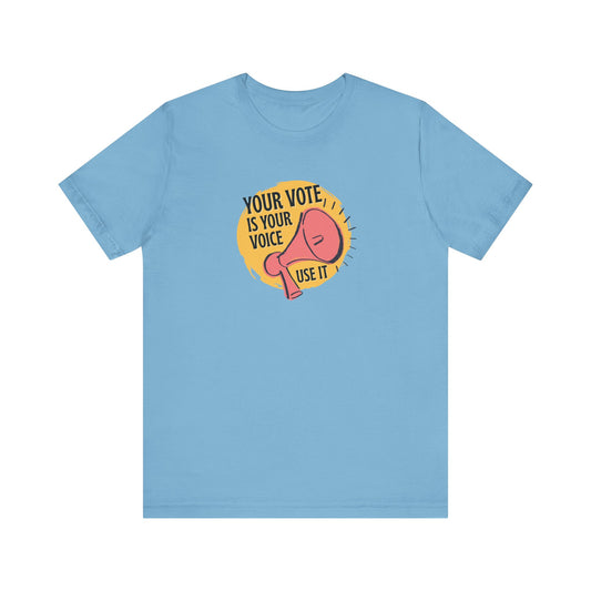 Light blue t-shirt with a coral megaphone graphic over bright yellow circle and black text "your vote is your voice, use it" 