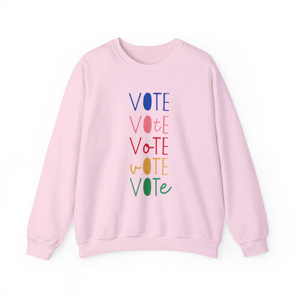 A light pink crewneck sweatshirt featuring a vertical graphic print of the word 'VOTE' repeated five times in alternating colors: blue, pink, red, yellow, and green.
