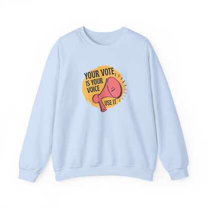 Light blue sweatshirt with a coral megaphone graphic against a bright yellow circle and black text "your vote is your voice, use it"