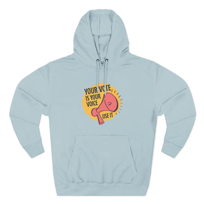 Light blue hoodie with coral megaphone graphic against a bright yellow circle and black text "your vote is your voice, use it"
