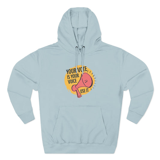 Light blue hoodie with coral megaphone graphic against a bright yellow circle and black text "your vote is your voice, use it"