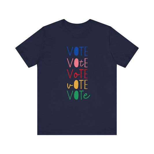 A navy blue short-sleeve t-shirt with a vertical graphic on the chest spelling 'VOTE' in alternating bright colors (blue, pink, red, yellow, green) with oval letterforms, shown on a plain white background.