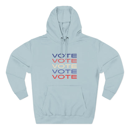 A light blue pullover hoodie with a front kangaroo pocket and drawstring hood, featuring a stacked 'VOTE' graphic in blue, red, and cream on the chest, displayed on a clean white background.