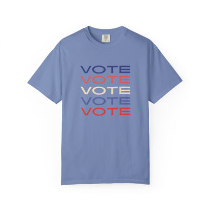 A blue short-sleeve crewneck t-shirt featuring a stacked graphic print of the word 'VOTE' in blue, red, and beige, displayed on a clean white background.