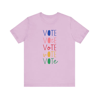 A light purple short-sleeve t-shirt with a vertical graphic on the chest spelling 'VOTE' in alternating bright colors (blue, pink, red, yellow, green) with oval letterforms, shown on a plain white background.