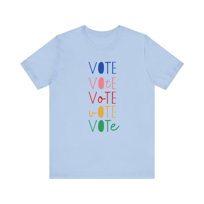 A light blue short-sleeve t-shirt with a vertical graphic on the chest spelling 'VOTE' in alternating bright colors (blue, pink, red, yellow, green) with oval letterforms, shown on a plain white background.