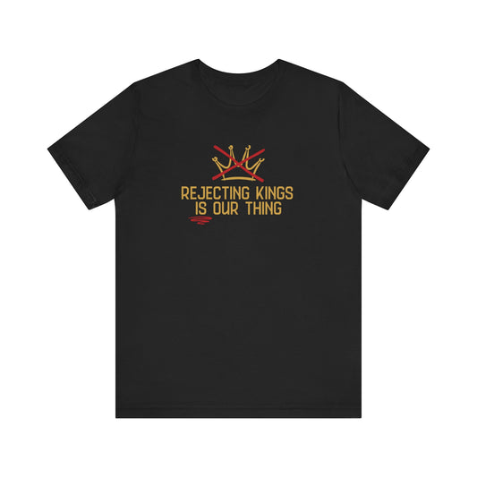 Black t-shirt with a gold graphic sketch of a brown with a red X over it and gold words underneath "Rejecting Kings Is Our Thing" 