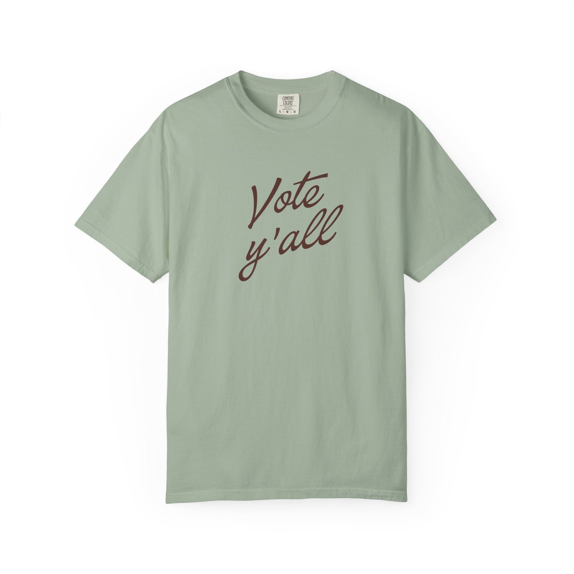 A short-sleeve crewneck t-shirt in a light green color, featuring the phrase 'Vote y'all' printed in brown cursive script across the chest, displayed on a clean white background.