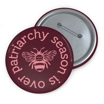 Maroon pin button with pink "patriarchy season is over" text circling around a queen bee graphic 