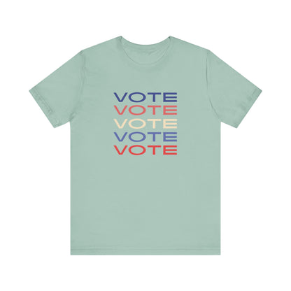 A light green short-sleeve crewneck t-shirt featuring a stacked graphic print of the word 'VOTE' in blue, red, and cream on the chest.